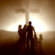 a family stands outside in front of a cross as the sun sets