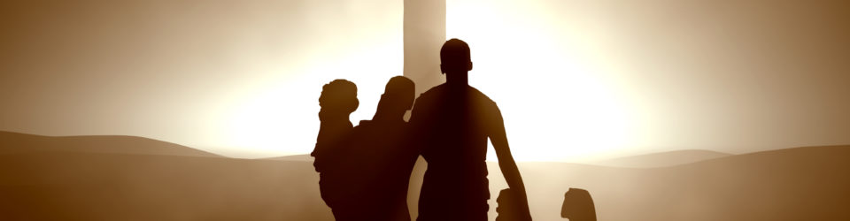 a family stands outside in front of a cross as the sun sets